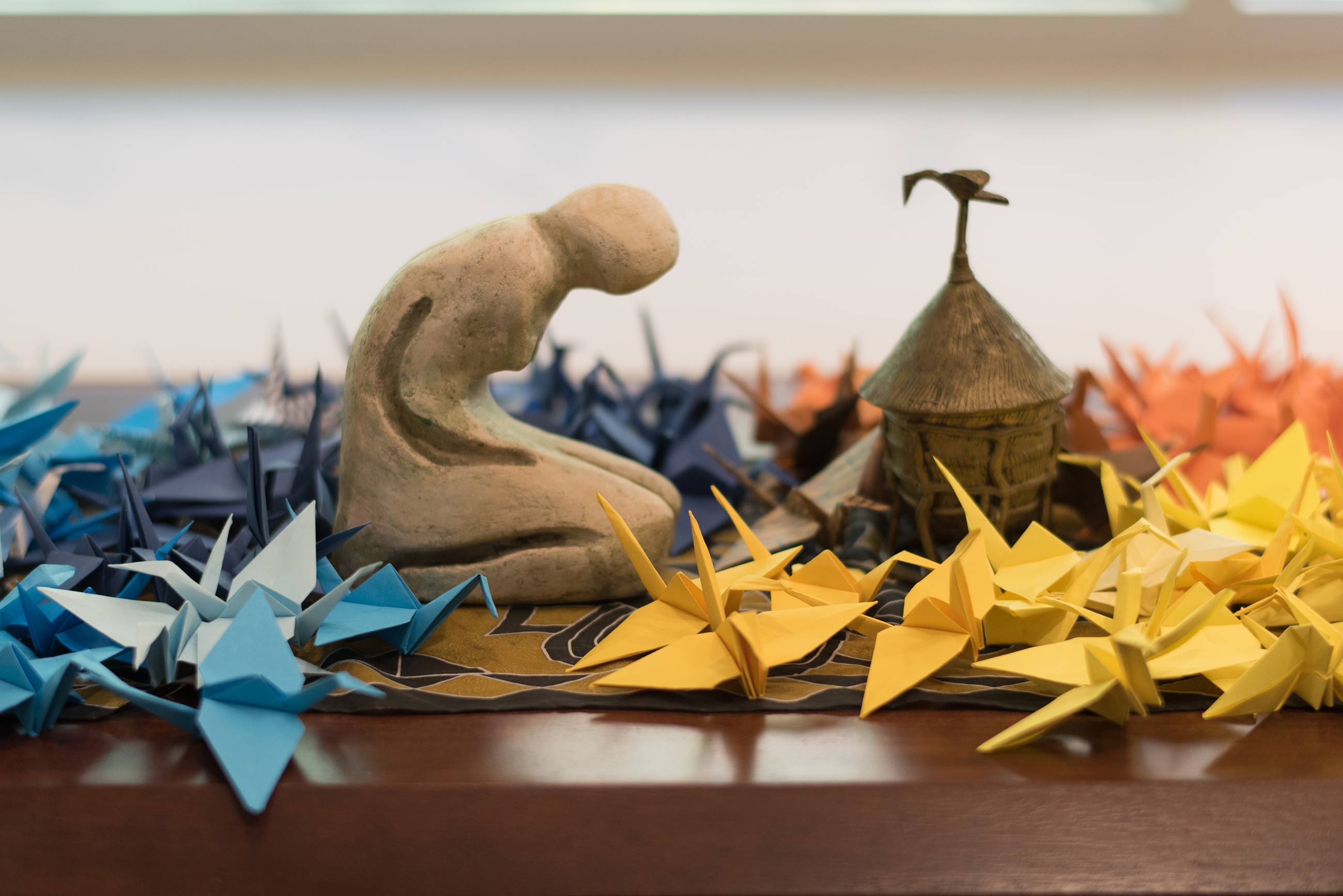 Small statue kneeling among multi-colored paper cranes