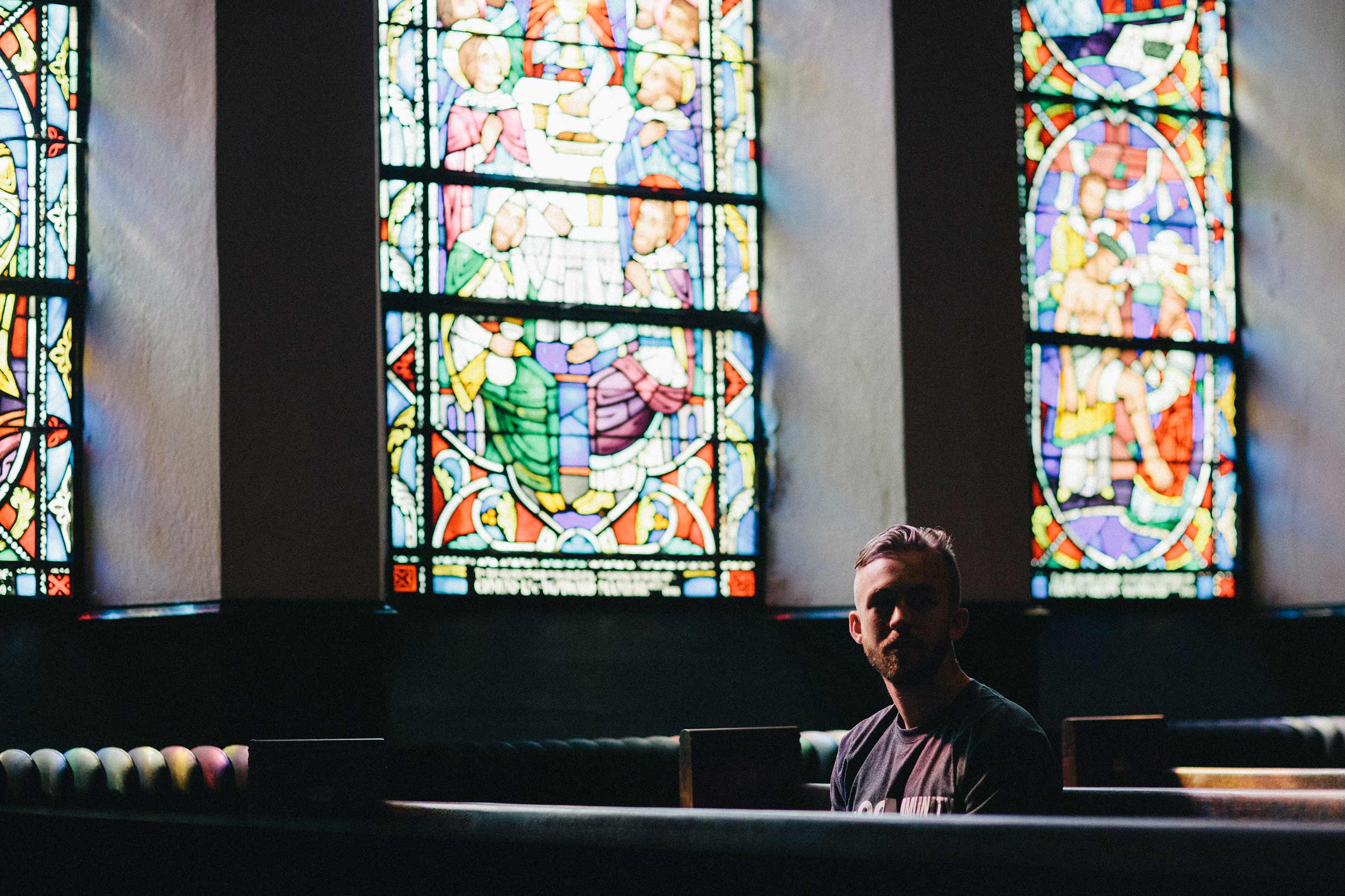 Man sitting in pews beneath large stained glass windows
