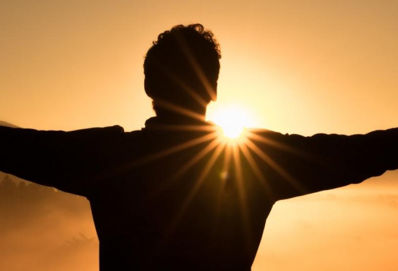 man in shadow with arms spread wide facing sunrise