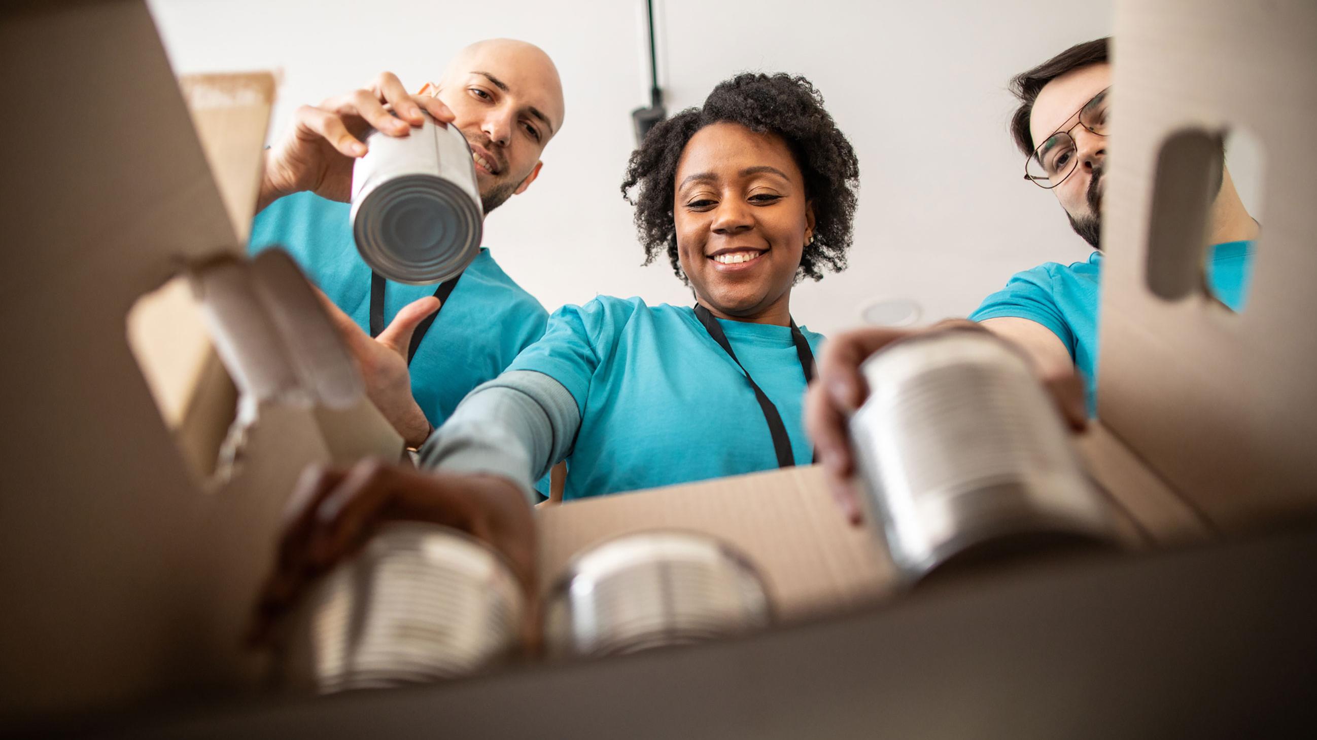 Three people happily loading cans into a box