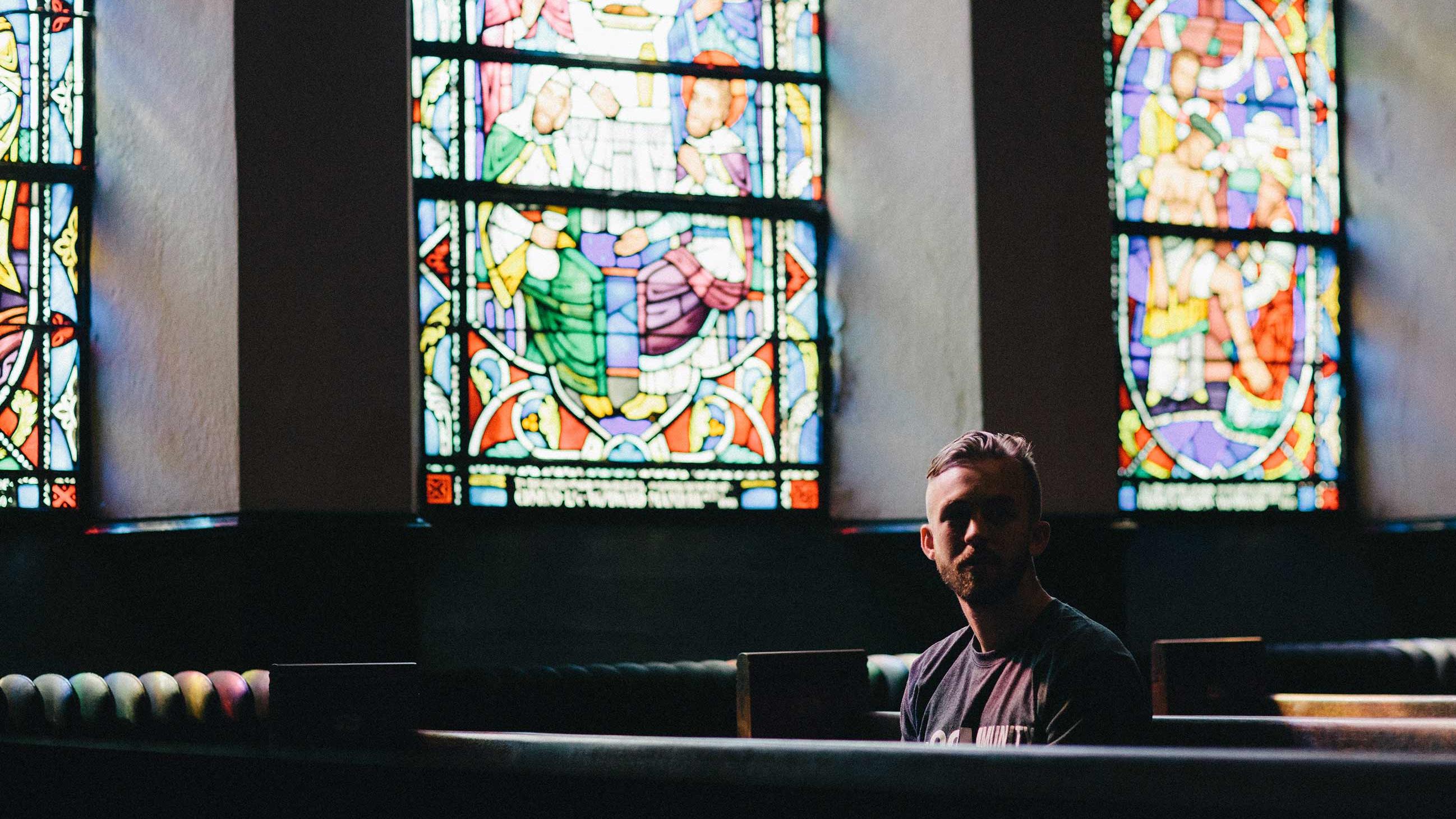 Man sitting in pews beneath large stained glass windows