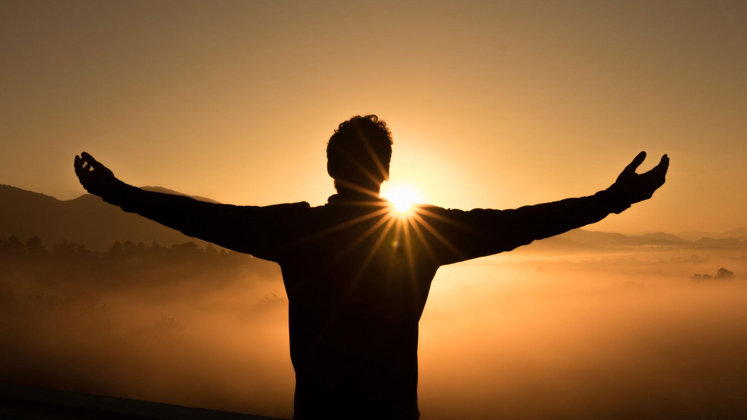 Person with open arms silhouetted against the sun