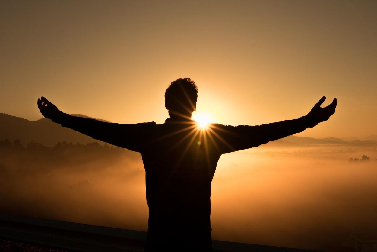 man in shadow with arms spread wide facing sunrise