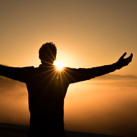Person with open arms silhouetted against the sun